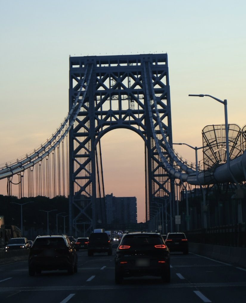 Cars heading toward a steel suspension bridge tower at dusk