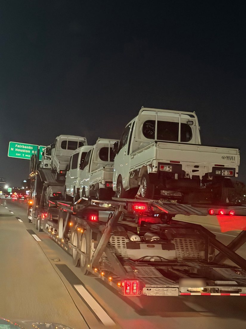 A car carrier loaded with small white kei trucks on a highway at night